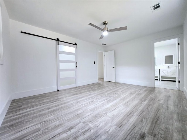 unfurnished bedroom with visible vents, ensuite bath, a barn door, light wood-style floors, and baseboards