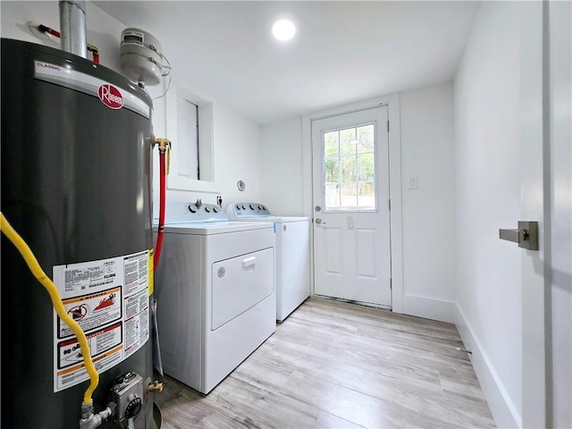 clothes washing area featuring baseboards, washing machine and clothes dryer, laundry area, light wood-style flooring, and gas water heater