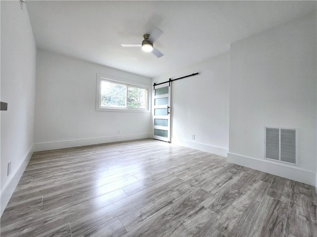 spare room with visible vents, a ceiling fan, wood finished floors, a barn door, and baseboards