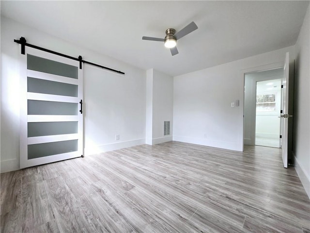 empty room featuring a ceiling fan, wood finished floors, visible vents, baseboards, and a barn door