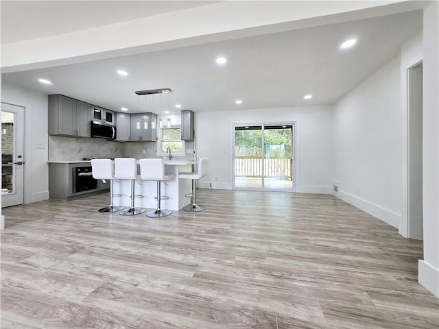 kitchen featuring a kitchen island, a kitchen bar, decorative backsplash, gray cabinets, and appliances with stainless steel finishes