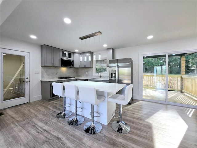 kitchen with wood finished floors, a breakfast bar, gray cabinets, a sink, and stainless steel appliances