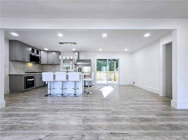 kitchen with a breakfast bar area, light wood finished floors, gray cabinetry, decorative backsplash, and appliances with stainless steel finishes