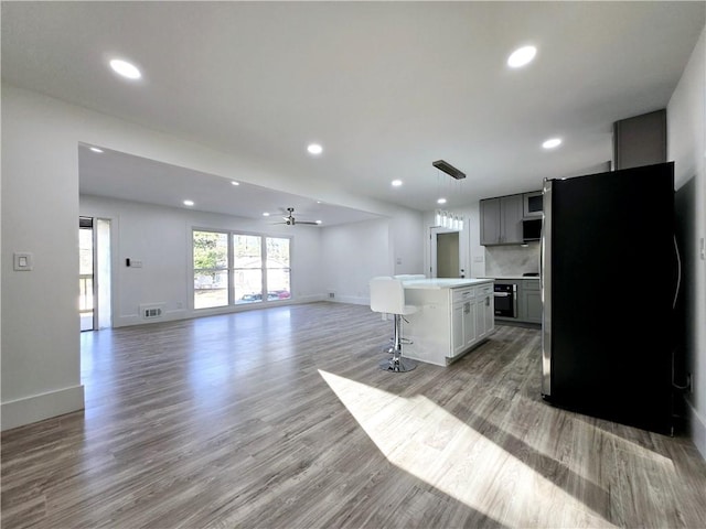 kitchen featuring visible vents, open floor plan, light countertops, a kitchen breakfast bar, and freestanding refrigerator