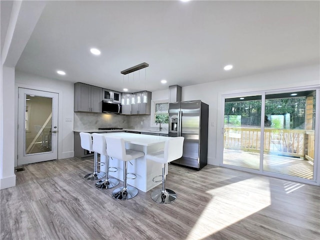 kitchen with decorative backsplash, light countertops, appliances with stainless steel finishes, light wood-type flooring, and a center island