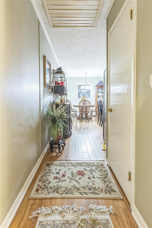 hallway with baseboards, light wood-style flooring, and a notable chandelier