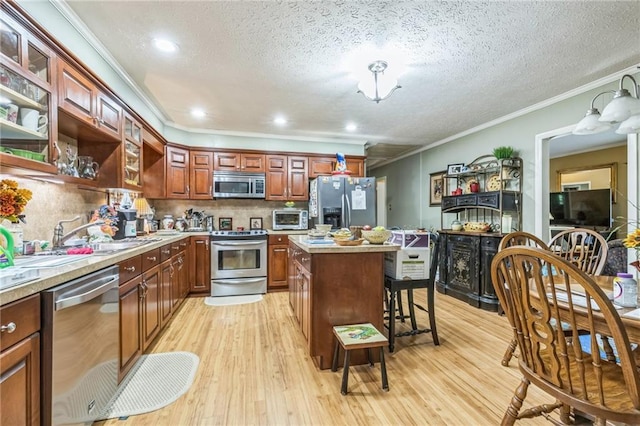 kitchen with light wood-style floors, ornamental molding, a sink, and appliances with stainless steel finishes