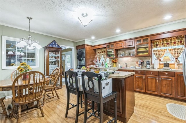 kitchen with a kitchen island, light wood-type flooring, light countertops, a textured ceiling, and stacked washer / drying machine