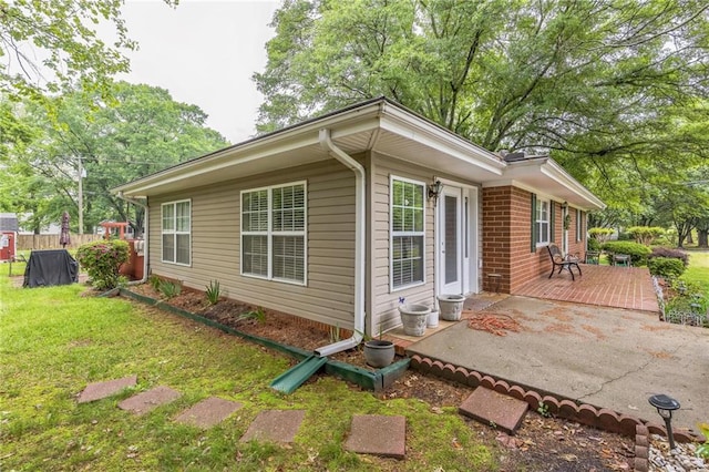 view of property exterior featuring a lawn, a wooden deck, a patio area, brick siding, and fence