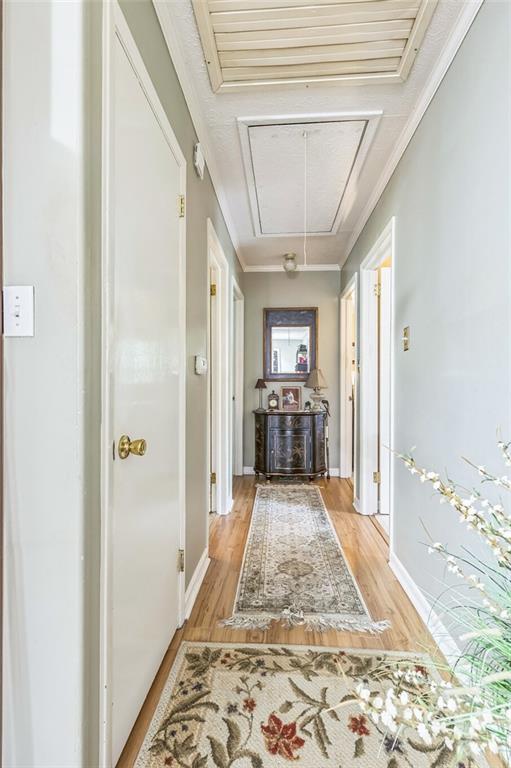 hallway with light wood-type flooring, attic access, and baseboards