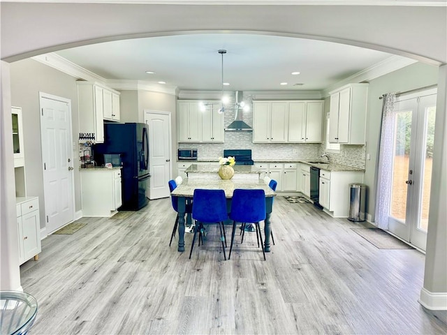 kitchen with arched walkways, black appliances, wall chimney range hood, and backsplash