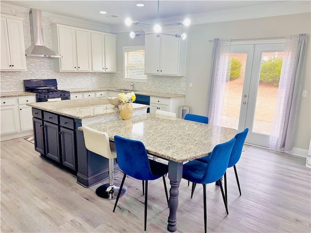 kitchen featuring white cabinets, ornamental molding, french doors, wall chimney range hood, and gas stove