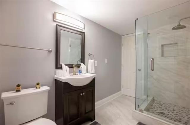 full bathroom featuring baseboards, a shower stall, toilet, and vanity