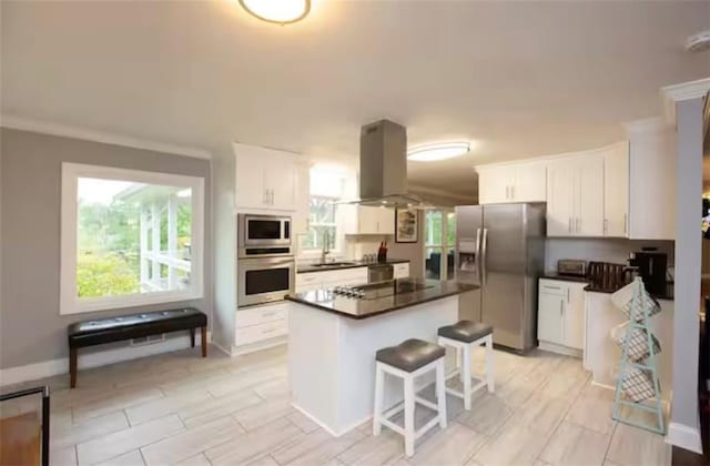 kitchen featuring dark countertops, appliances with stainless steel finishes, island exhaust hood, white cabinetry, and a sink