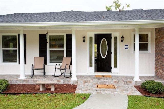 doorway to property with brick siding, a porch, and roof with shingles