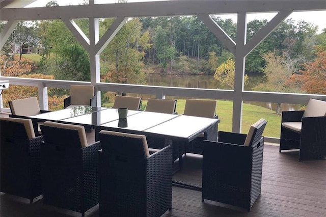 wooden terrace featuring outdoor dining area, a water view, and a wooded view