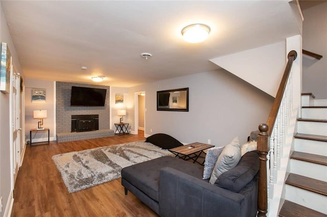 living room featuring a brick fireplace, stairs, baseboards, and wood finished floors