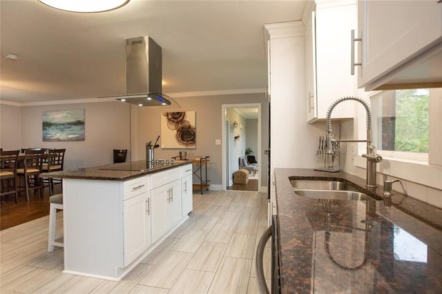 kitchen featuring black electric cooktop, island range hood, a sink, ornamental molding, and dark stone counters