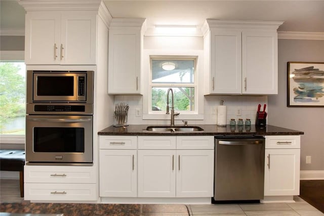 kitchen with dark stone counters, stainless steel appliances, ornamental molding, and a sink