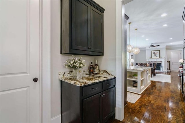 bar featuring dark hardwood / wood-style floors, a fireplace, hanging light fixtures, light stone counters, and dark brown cabinetry