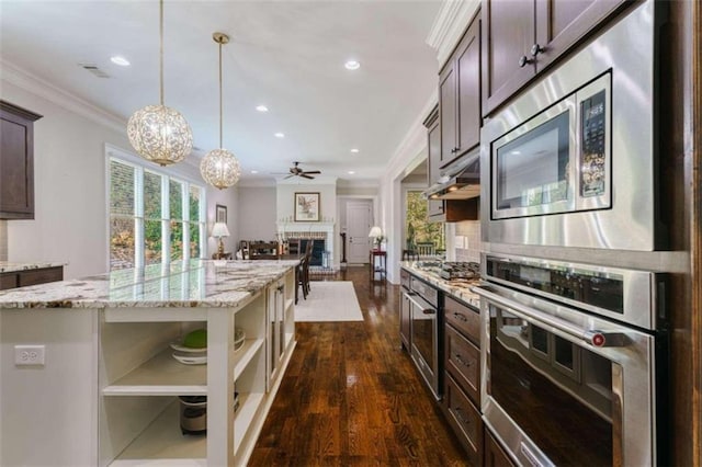 kitchen with appliances with stainless steel finishes, pendant lighting, a fireplace, light stone countertops, and dark brown cabinets