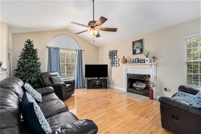 living room with ceiling fan, a fireplace with flush hearth, vaulted ceiling, baseboards, and light wood-style floors