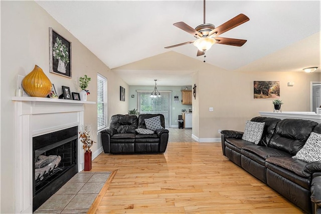 living room with light wood finished floors, a ceiling fan, baseboards, a fireplace with flush hearth, and vaulted ceiling