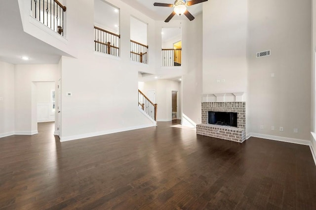 unfurnished living room with a high ceiling, ceiling fan, dark hardwood / wood-style floors, and a brick fireplace