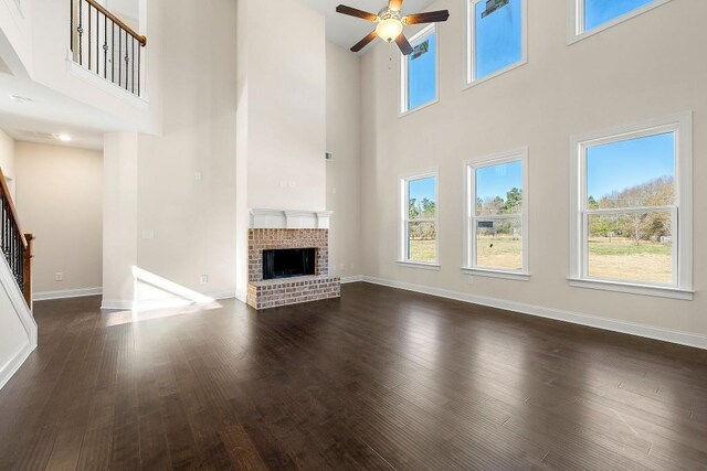 unfurnished living room with a towering ceiling, ceiling fan, dark hardwood / wood-style floors, and a brick fireplace