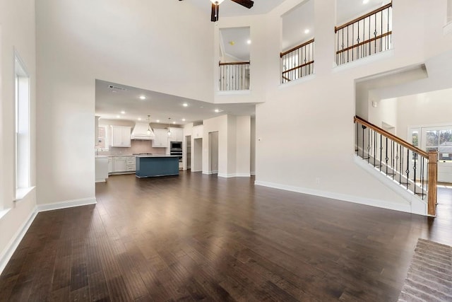 unfurnished living room featuring ceiling fan, dark hardwood / wood-style floors, and a towering ceiling