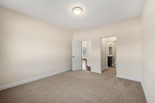 unfurnished bedroom featuring light colored carpet and ensuite bath