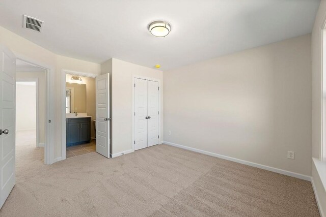 unfurnished bedroom featuring ensuite bathroom, a closet, and light carpet