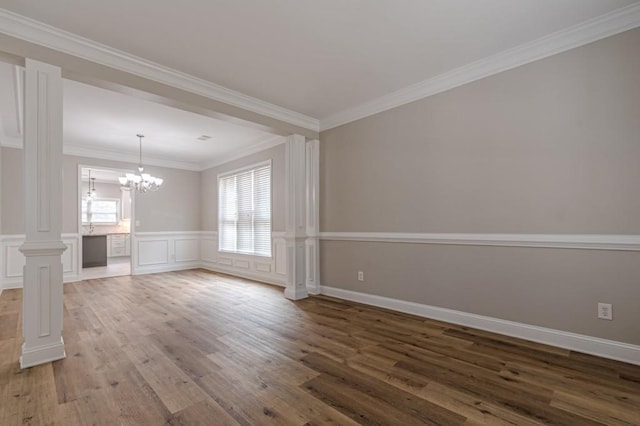 empty room with crown molding, decorative columns, a chandelier, and hardwood / wood-style flooring