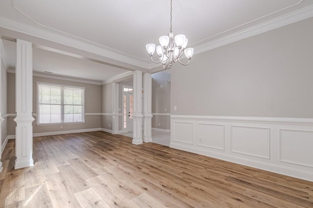 spare room featuring ornate columns, light hardwood / wood-style flooring, crown molding, and a chandelier