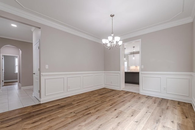 spare room with light wood-type flooring, ornamental molding, and an inviting chandelier