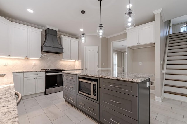 kitchen with appliances with stainless steel finishes, light stone counters, white cabinets, decorative light fixtures, and premium range hood