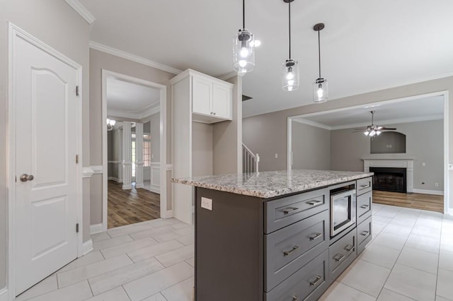 kitchen featuring hanging light fixtures, white cabinets, stainless steel microwave, a center island, and ceiling fan