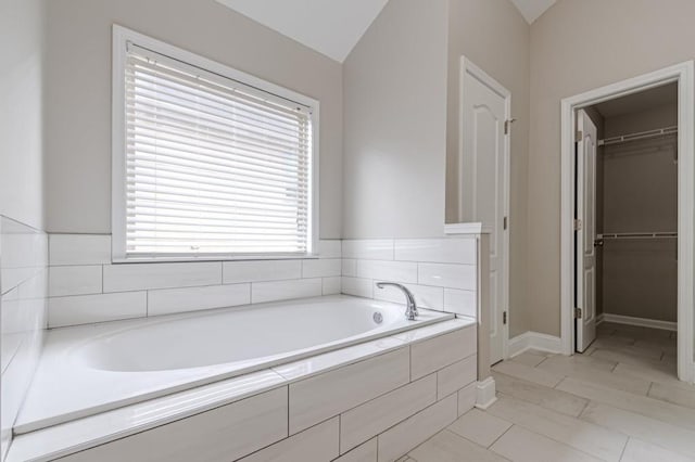 bathroom featuring a wealth of natural light, vaulted ceiling, tiled bath, and tile patterned floors