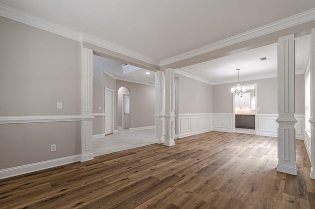 empty room featuring ornate columns, ornamental molding, a chandelier, and hardwood / wood-style floors