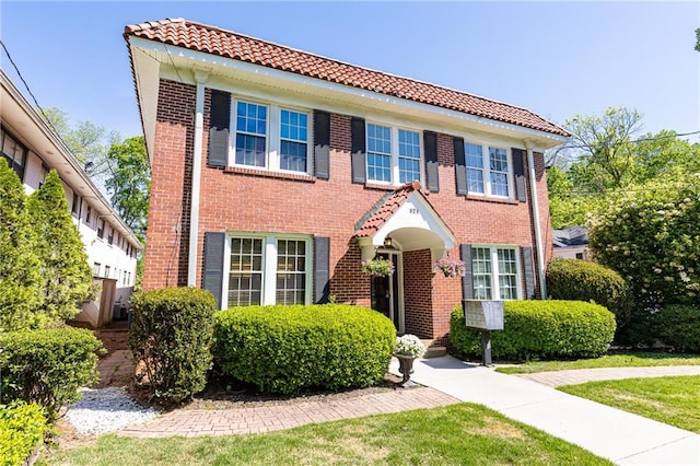 view of front of home with brick siding, a tiled roof, and a front yard