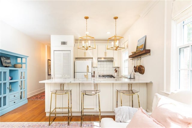kitchen featuring under cabinet range hood, visible vents, freestanding refrigerator, a peninsula, and tasteful backsplash