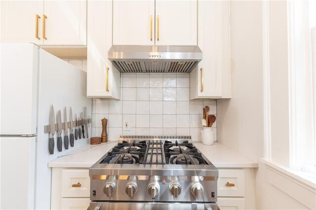 kitchen featuring freestanding refrigerator, high end stove, backsplash, white cabinetry, and under cabinet range hood