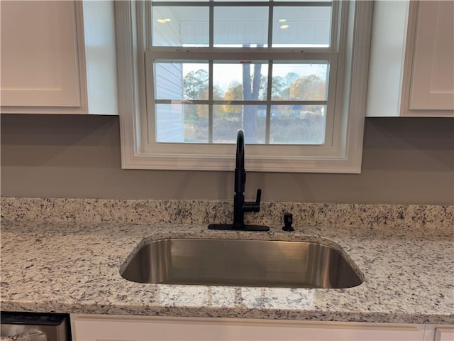 kitchen with light stone countertops, sink, dark wood-type flooring, stainless steel dishwasher, and white cabinets