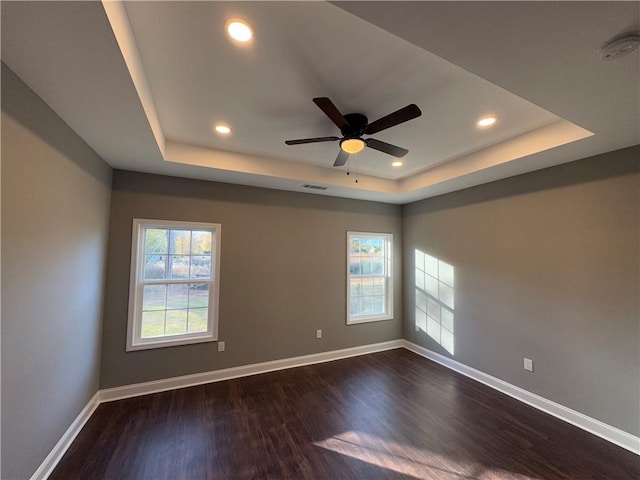 empty room featuring a tray ceiling, ceiling fan, and dark wood-type flooring