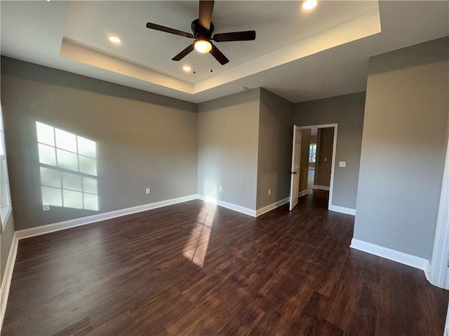 empty room with a tray ceiling, ceiling fan, and dark wood-type flooring