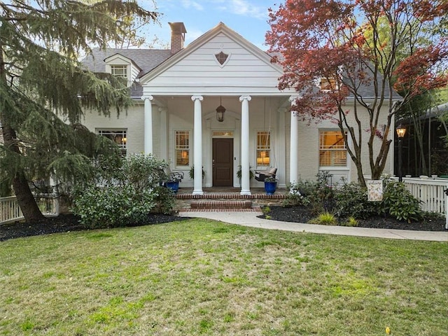 greek revival inspired property with brick siding, a porch, a chimney, and a front lawn