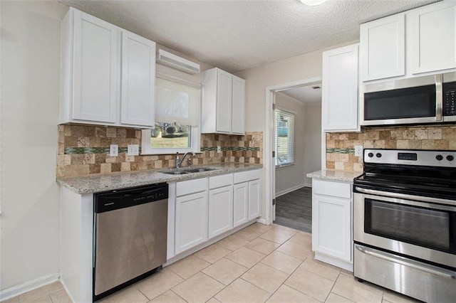 kitchen with a sink, backsplash, white cabinetry, appliances with stainless steel finishes, and light stone countertops