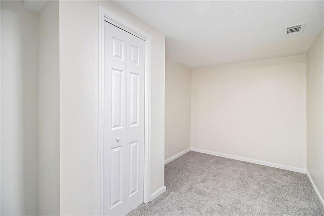 carpeted spare room featuring baseboards, visible vents, and a textured ceiling