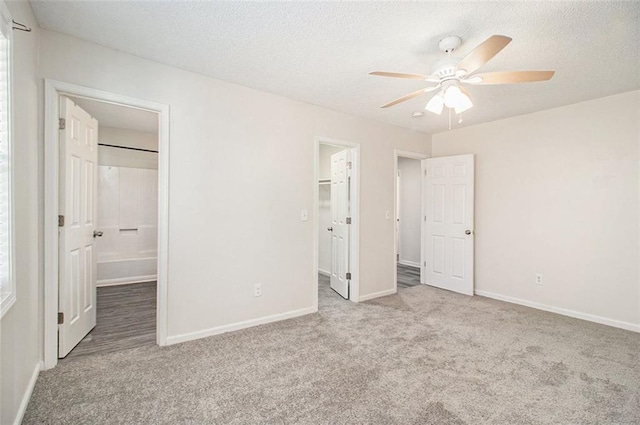 unfurnished bedroom with a walk in closet, carpet flooring, baseboards, and a textured ceiling