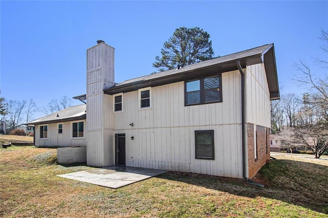 rear view of house featuring a patio area, a lawn, and a chimney